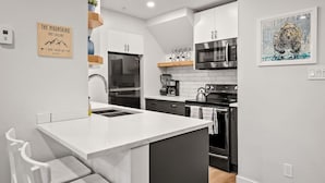 A modern kitchen with white cabinetry, a central island, stainless steel appliances, and a decorative bear painting.