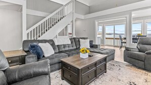 A spacious living room with a grey sectional sofa, a wooden coffee table, and a staircase leading to an upper level. - Beach House · Beautiful Beachfront House, Close to Burlington! (Colchester)