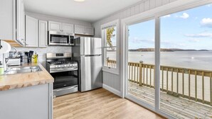 A modern kitchen with stainless steel appliances, a wooden countertop, and a large window overlooking a body of water. - Beach House · Beautiful Beachfront House, Close to Burlington! (Colchester)