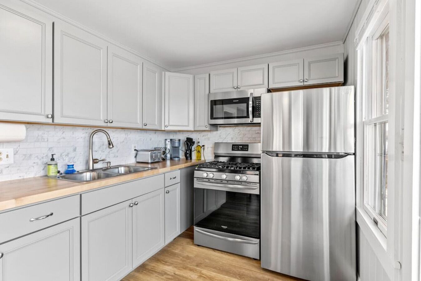 A modern kitchen with white cabinetry, stainless steel appliances, and a wooden countertop.