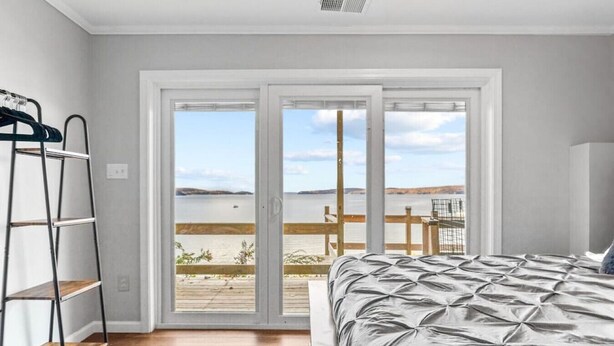 A bedroom with a bed, a ladder, and a view of a body of water through a sliding door. - Beach House · Beautiful Beachfront House, Close to Burlington! (Colchester)