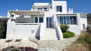 Un bâtiment blanc avec un escalier menant à un balcon, entouré de verdure et de fleurs.