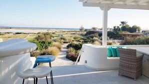 Une terrasse dotée de mobilier blanc, offrant une vue sur la plage, et un espace abrité avec un fauteuil en osier.