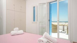 Une chambre à coucher comprenant un lit, une armoire et une porte-fenêtre coulissante donnant sur un balcon avec vue sur la plage.
