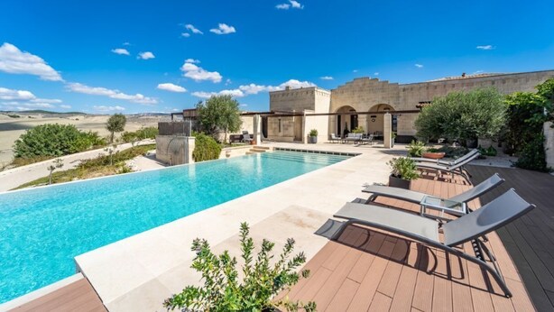 A swimming pool with lounge chairs and a water feature, surrounded by a patio and a building with arched windows.