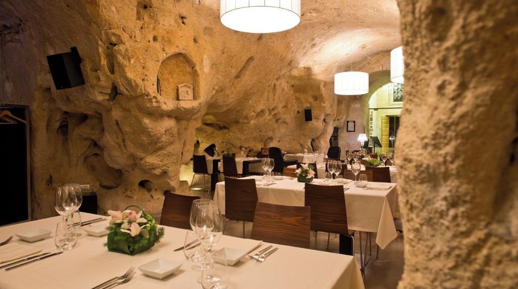 A restaurant with tables set for dining, stone walls, and a chandelier.