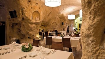 A restaurant with tables set for dining, stone walls, and a chandelier.