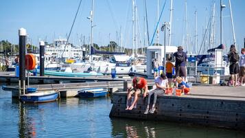 A marina with boats docked, people sitting on a dock, and a clear sky.