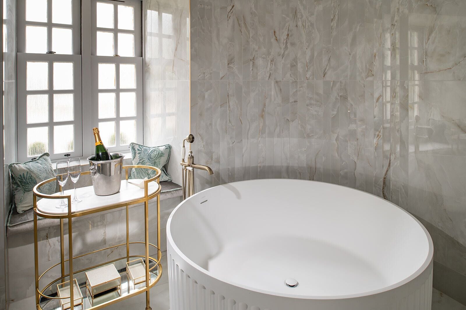 Un baño moderno con una bañera independiente, un tocador con marco dorado y una ventana con vistas a zonas verdes.
