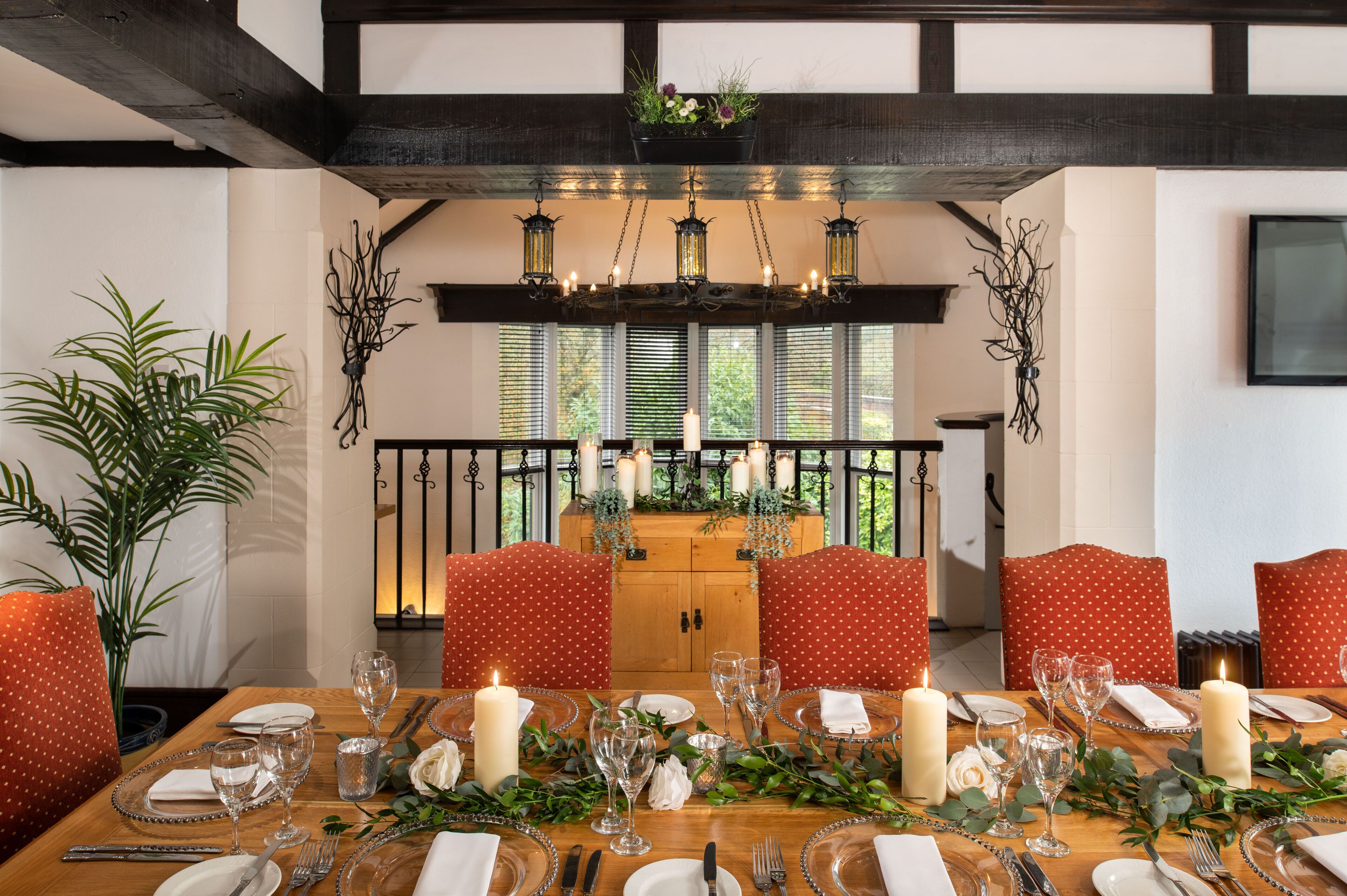 Una mesa de comedor decorada con velas, cristalería y un centro de hojas verdes.