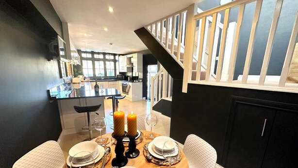 Een eetgedeelte met een ronde tafel voor vier personen, met witte stoelen en een zwart kaarsdecoratie.