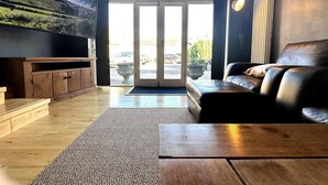 Een ruime woonkamer met een grote televisie, leren bank, houten salontafel en uitzicht door de glazen deuren.