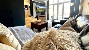 Een moderne woonkamer met een bank, een salontafel en een televisie. Er is een raam met uitzicht op buiten.