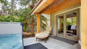 Un espacio al aire libre cubierto con un jacuzzi, una silla y un ventanal corredero que da a un área interior.