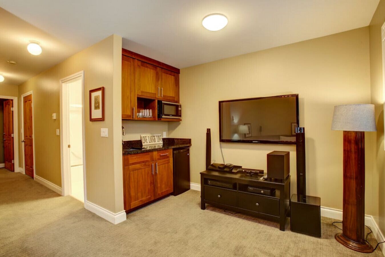 A well-lit hallway with wooden cabinets, a microwave, and a flat-screen TV mounted on the wall.