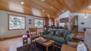 Ein geräumiges Wohnzimmer mit Holzboden, großen Fenstern, einem Kamin und einer gemütlichen Sitzecke.