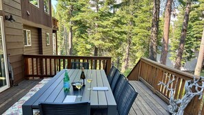 Eine Holzterrasse mit Tisch und Stühlen, umgeben von hohen Bäumen.
