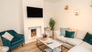 A modern living room with a fireplace, a flat-screen TV, and a coffee table. - Alma Cottage (Buxton)
