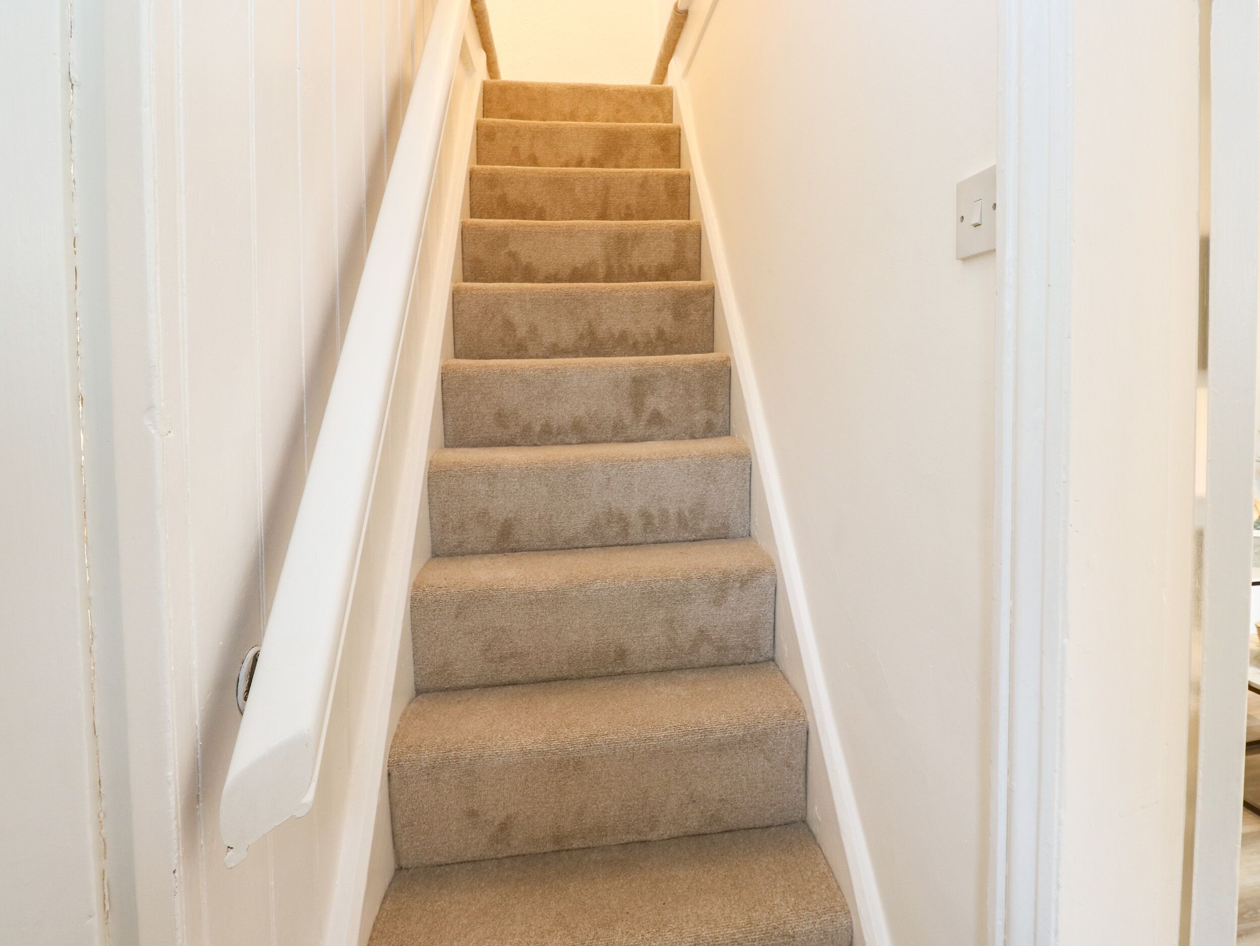 A carpeted staircase with white walls and a white handrail.
