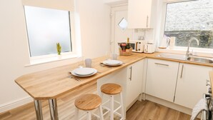 A modern kitchen with a wooden countertop, white cabinets, a sink, and two stools. - Alma Cottage (Buxton)