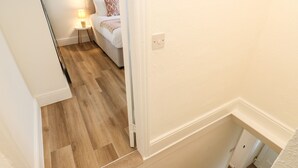 A staircase with carpeted steps leading to a bedroom with a bed, a nightstand, and a lamp. - Alma Cottage (Buxton)
