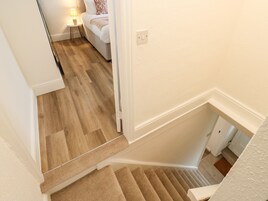 A staircase with carpeted steps leading to a bedroom with a bed, a nightstand, and a lamp.