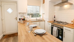A modern kitchen with a wooden countertop, stainless steel appliances, and a window providing a view of the outdoors. - Alma Cottage (Buxton)