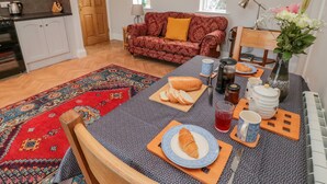 Een gezellige woonkamer met een bank, een eettafel gedekt met brood, een theepot en een bloevas.