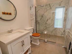 Une salle de bain avec une douche en marbre, des toilettes avec un abattant en bois, un lavabo et un miroir.