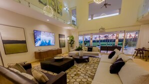 Un salon spacieux avec un plafond haut, un grand téléviseur à écran plat, un ensemble de canapés et une vue sur un terrain de golf grâce à de grandes fenêtres.