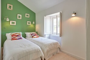 A bedroom with two beds, green walls, and a window with a view.