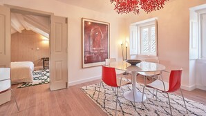 Un comedor con una mesa redonda, sillas rojas, una araña y un cuadro abstracto grande en la pared.