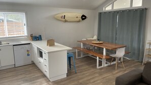 Een kleine keuken met een eethoek, een surfboard decoratie en een grijze gordijn.