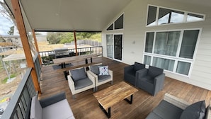 Een overdekt terras buiten, met houten vloer, rieten meubels en een barbecue.
