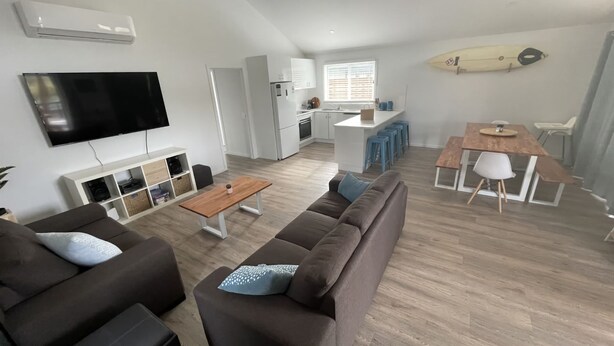 Een moderne woonkamer met een flatscreen televisie, een bank, een salontafel en een eethoek met een houten tafel en stoelen.