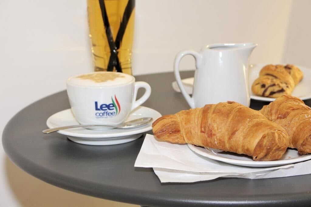 A table with a cup of coffee, a croissant, and a pitcher.