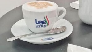 Una mano sosteniendo un croissant sobre una taza de café con una cuchara en un platito.