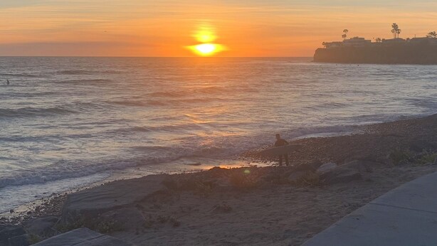 A beach scene with a sunset over the ocean, a person with a surfboard, and a rocky shoreline. - Pool & Oceanview, Spacious 4bdrm 2 1/2 ba in a very nice neighborhood. (San Diego)