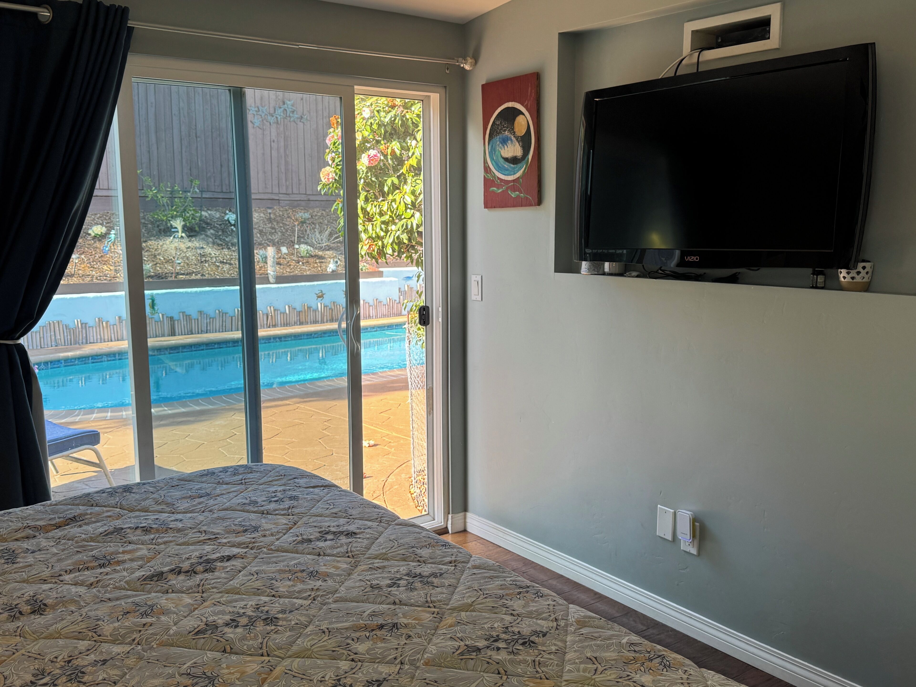 Un dormitorio con cama, televisor montado en la pared y puerta corrediza de vidrio que da a una zona de piscina.
