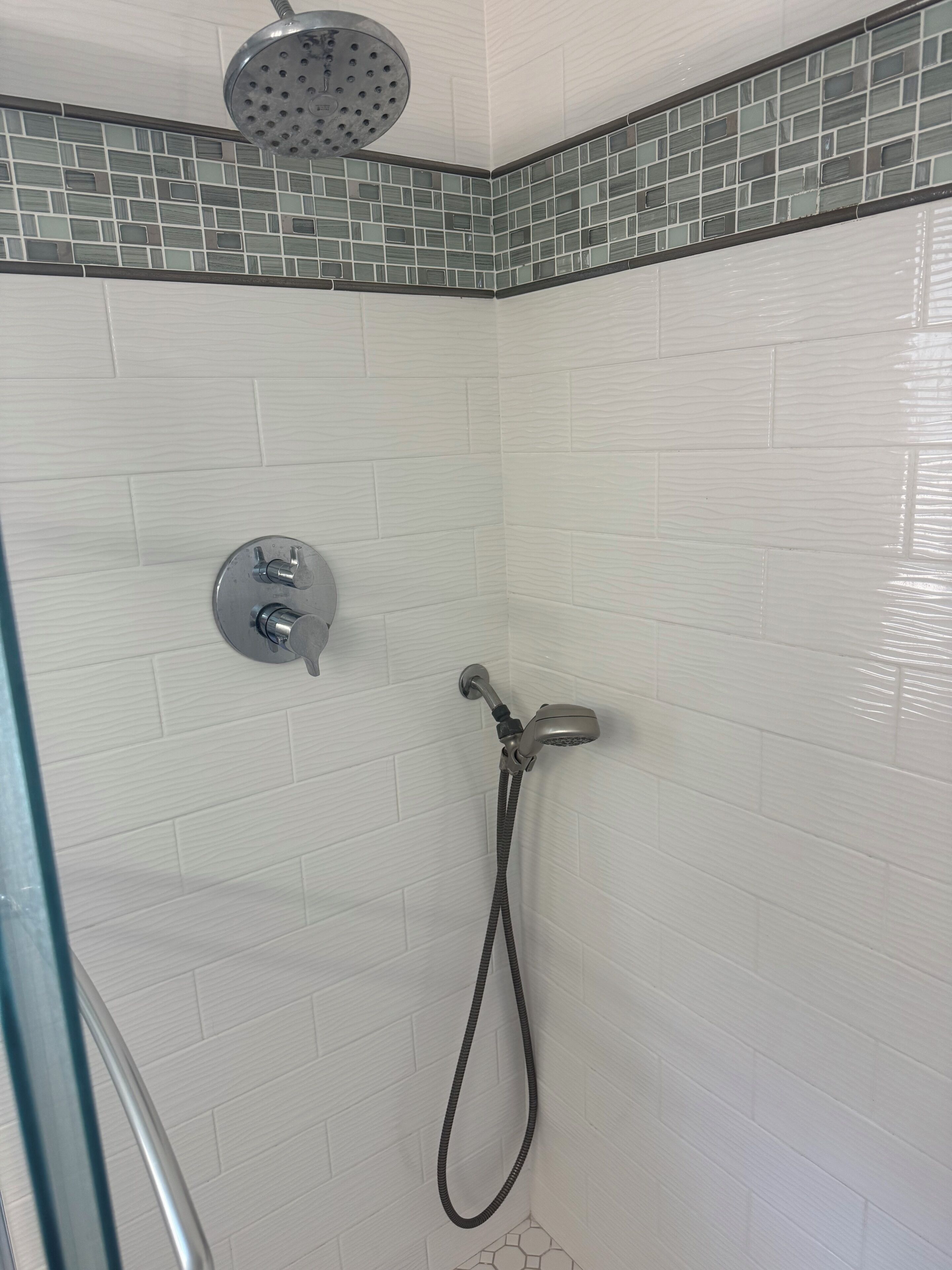 A shower area with a handheld showerhead and a wall-mounted faucet.