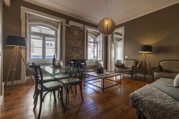 A spacious living area with a glass dining table, comfortable seating, a large window, and a cozy sofa.