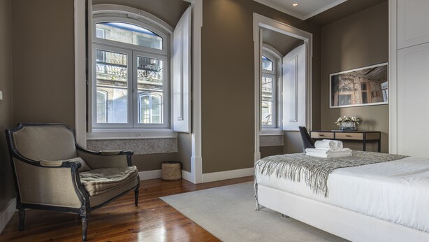 A bedroom with a large bed, a chair, a desk, and two windows with views of buildings. - Central São Paulo by Lisbon Heart (Lisboa)