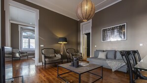 A living room with a wooden floor, a glass coffee table, and a grey sofa. There are two armchairs and a lamp. - Central São Paulo by Lisbon Heart (Lisboa)