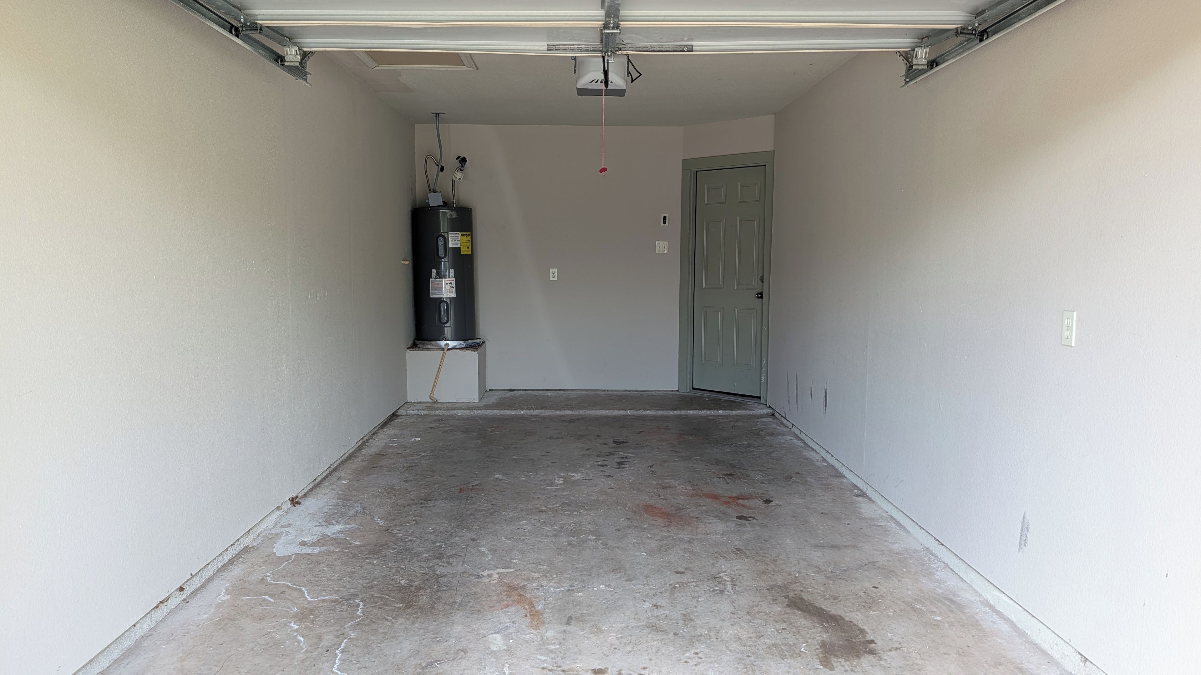 Un couloir étroit avec un chauffe-eau, une porte et un ventilateur de plafond.