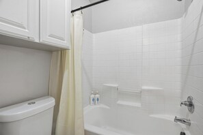 A bathroom with a toilet, shower, and two bottles of toiletries on the wall. - Spacious & Comfortable 3 Bedroom Home with Garage (Fort Worth)