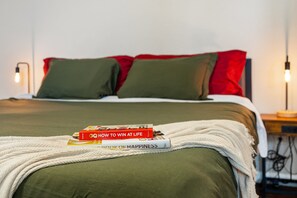 Una cama con ropa de cama verde, dos almohadas y un plaid blanco. Hay dos libros sobre la cama.