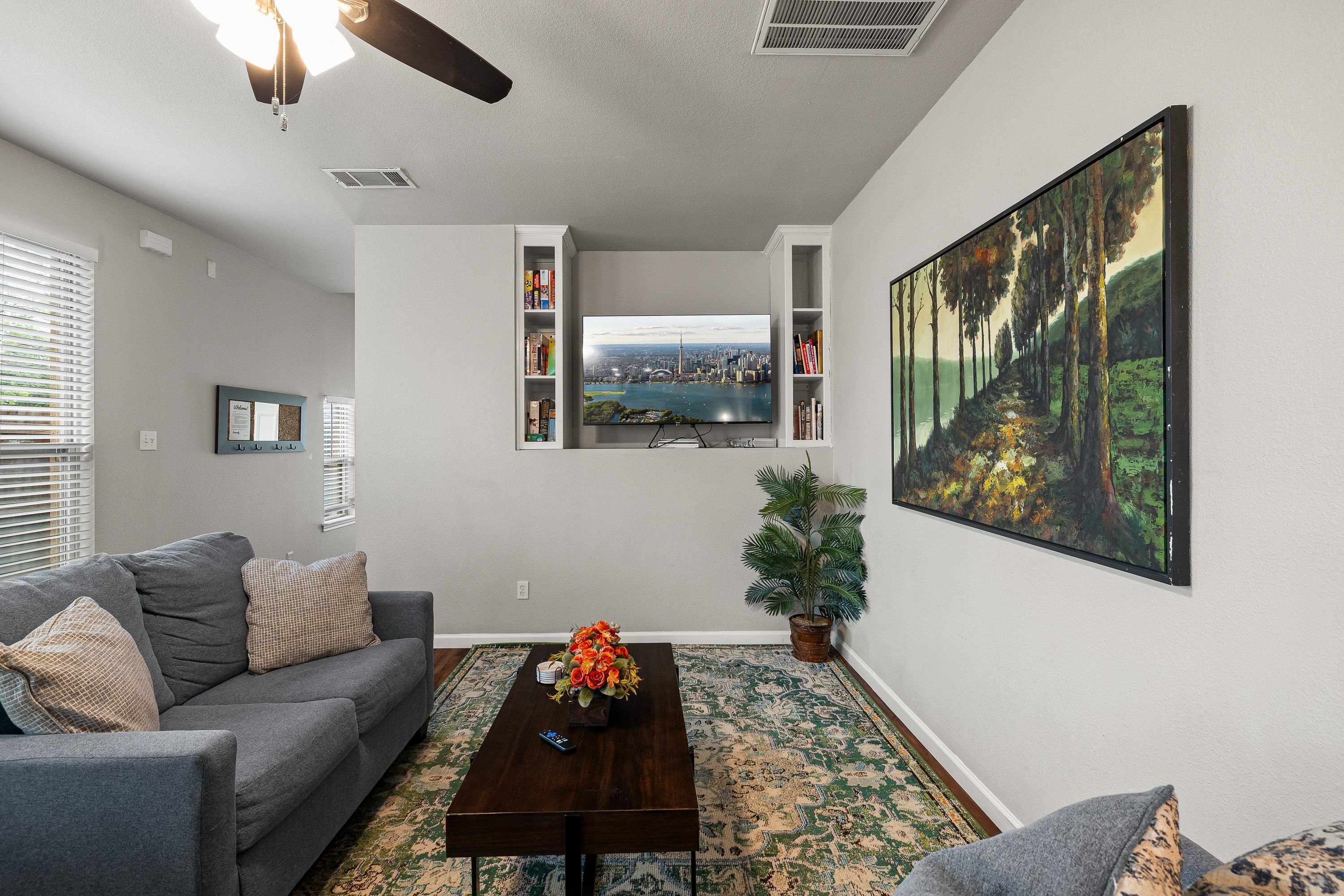 A living room with a gray sofa, a coffee table, a TV mounted on the wall, and a painting.