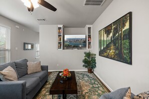 Una sala de estar con un sofá gris, una mesa de centro, un televisor montado en la pared y un cuadro.