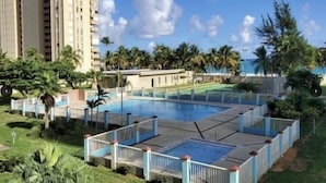 A swimming pool surrounded by a fence, with palm trees and a building in the background.