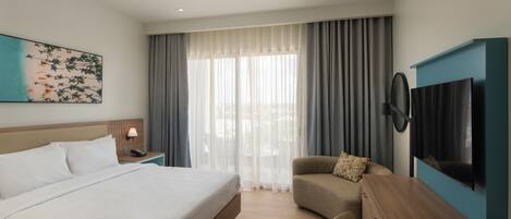 Een hotelkamer met een groot bed, een bureau, een stoel, een televisie, een schilderij aan de muur en een raam met gordijnen.